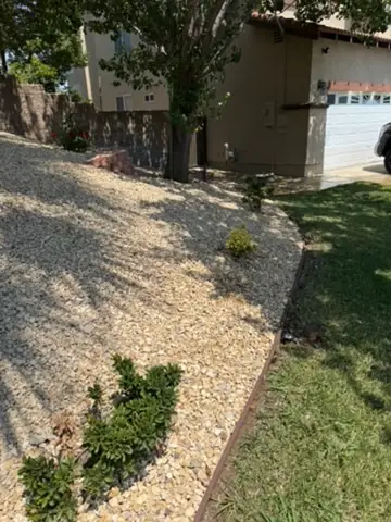Landscaped yard by Roth Landscaping in Orange County featuring gravel slope, strategically placed shrubs, and a modern home backdrop, showcasing services like custom yard design and installation of plants for aesthetic and functional outdoor spaces.